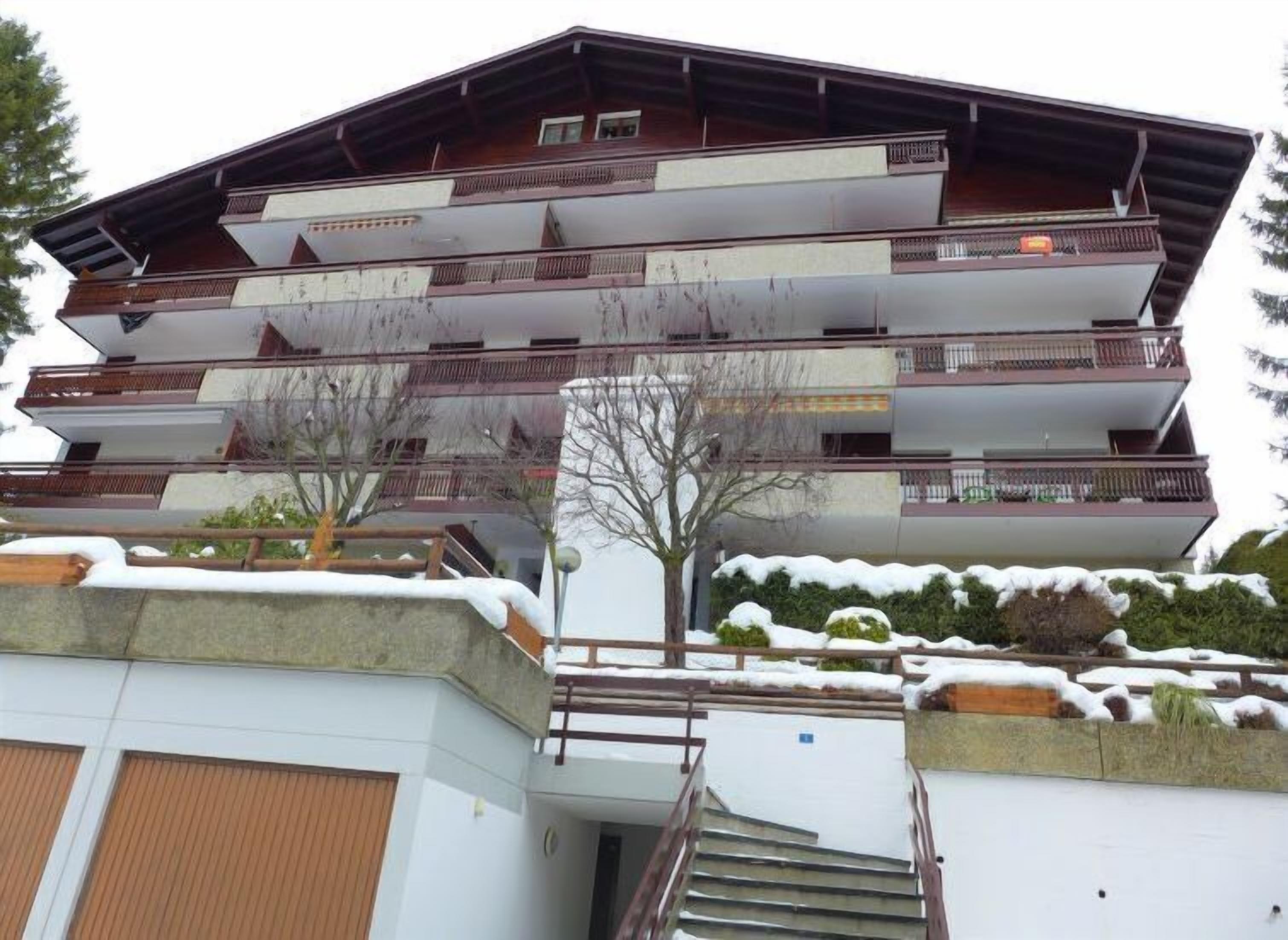 Un immeuble à plusieurs étages doté de balcons, d’un escalier et recouvert de neige sur le toit et au sol.