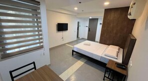Ein Hotelzimmer mit Bett, Fernseher, Schreibtisch und Fenster mit Jalousien.
