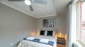 A bedroom with a bed, a ceiling fan, a zebra-patterned artwork, bedside lamps, and a window with curtains. - Windsor. Backyard Entertainer. Dubbo. (Dubbo)
