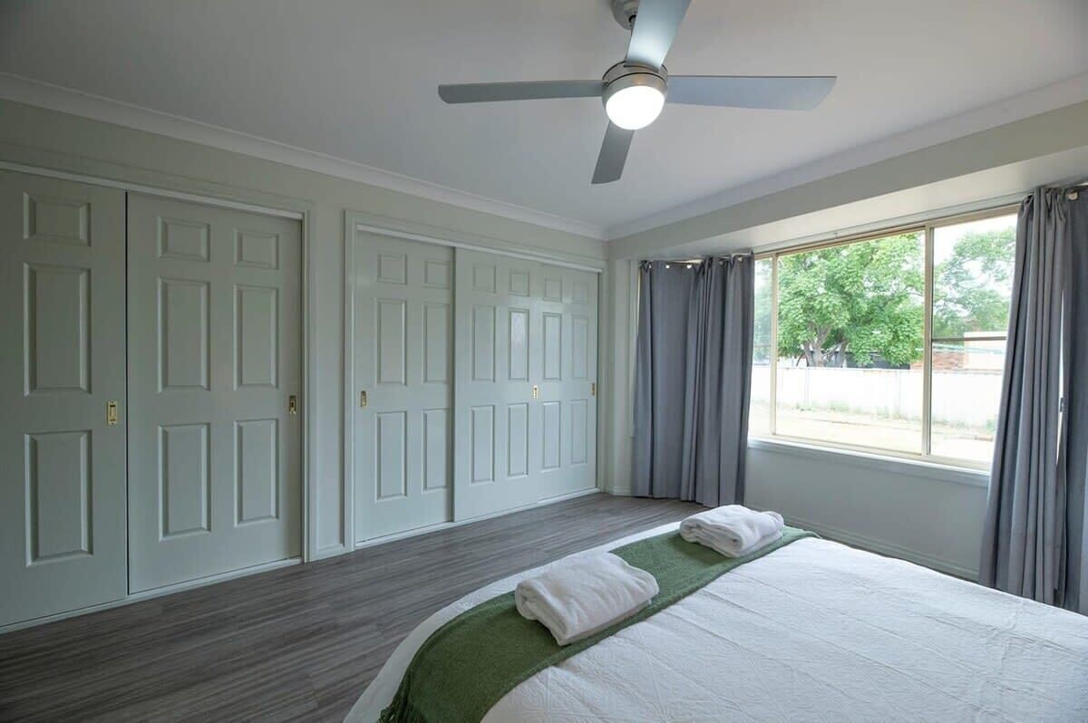 A bedroom with a bed, a ceiling fan, and a window with curtains.