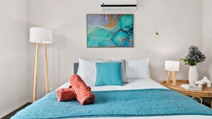 Una habitación de hotel con cama, un cuadro, una lámpara y una mesita de noche.