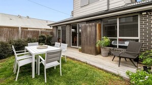 Una casa residencial con patio, una mesa de comedor con sillas y un pequeño jardín.