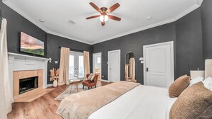 Un dormitorio con una cama grande, ventilador de techo, chimenea y televisión en la pared.