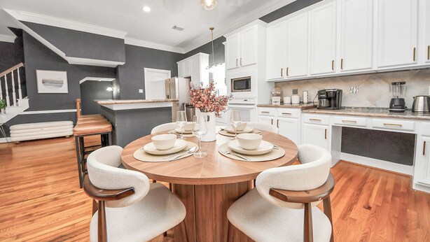Una cocina moderna con armarios blancos, una mesa de comedor de madera y una lámpara de araña.
