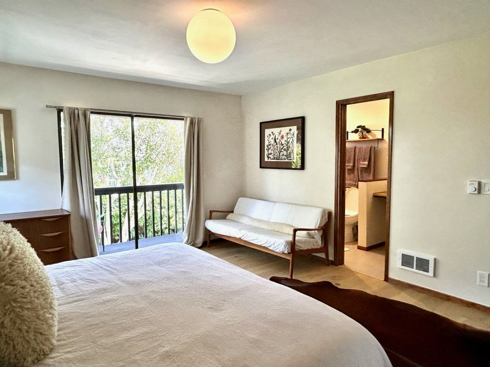 Une chambre à coucher avec un grand lit, un canapé, une fenêtre avec des rideaux, un tableau encadré et une armoire.