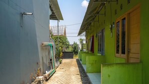 A narrow alleyway with a paved path, flanked by buildings with green and white walls, and a metal structure on the left. - OYO Life 93382 Gajayana Kost Female Only Syariah (Malang)