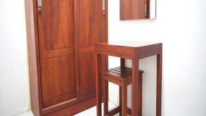 A wooden wardrobe with a mirror above it, a small wooden table, and a tiled floor. - OYO Life 93382 Gajayana Kost Female Only Syariah (Malang)