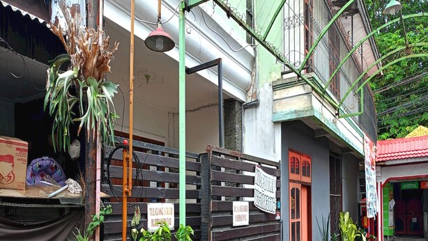 A narrow street with a row of potted plants and a signboard. - OYO Life 93382 Gajayana Kost Female Only Syariah (Malang)
