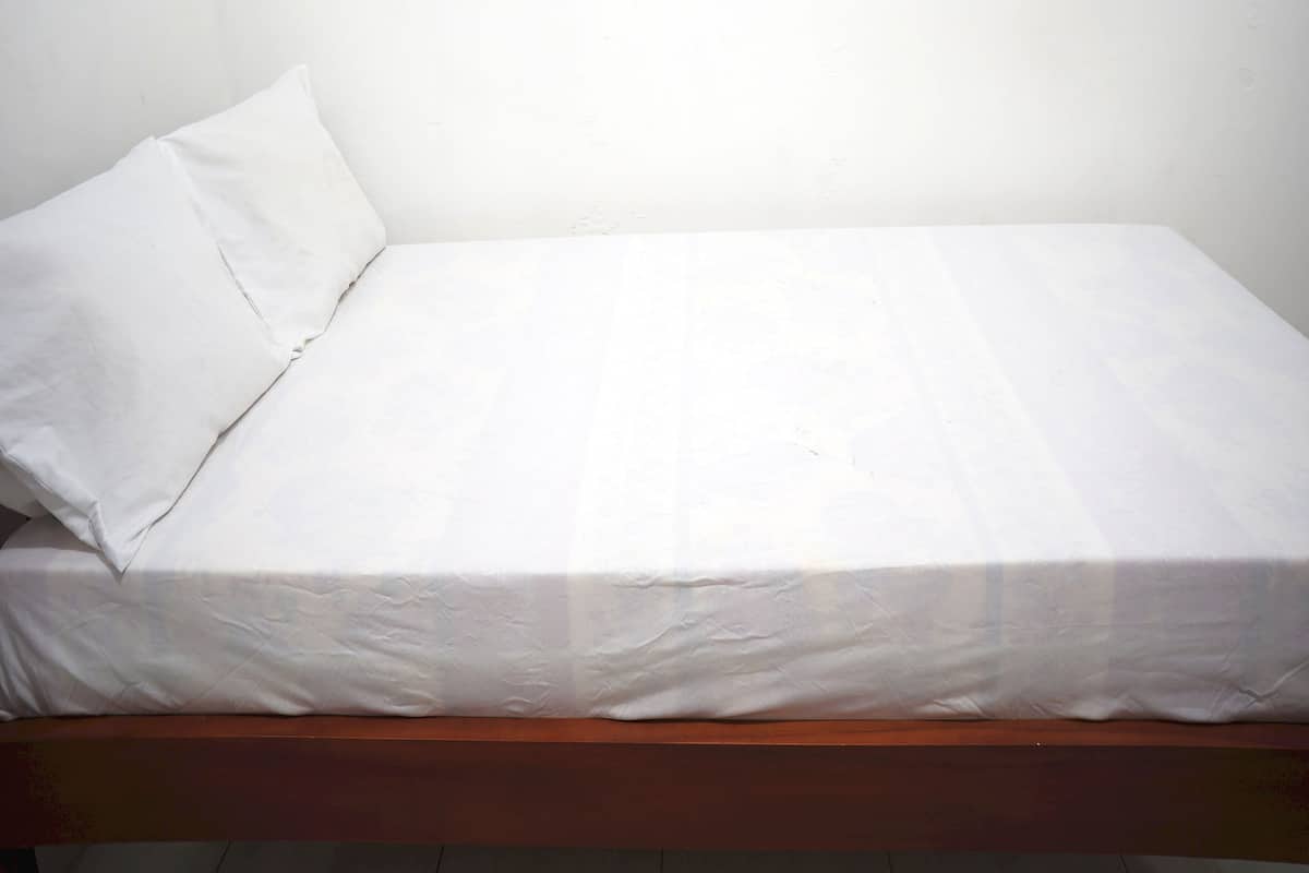 A single bed with a wooden frame and white bedding in a room with plain white walls.