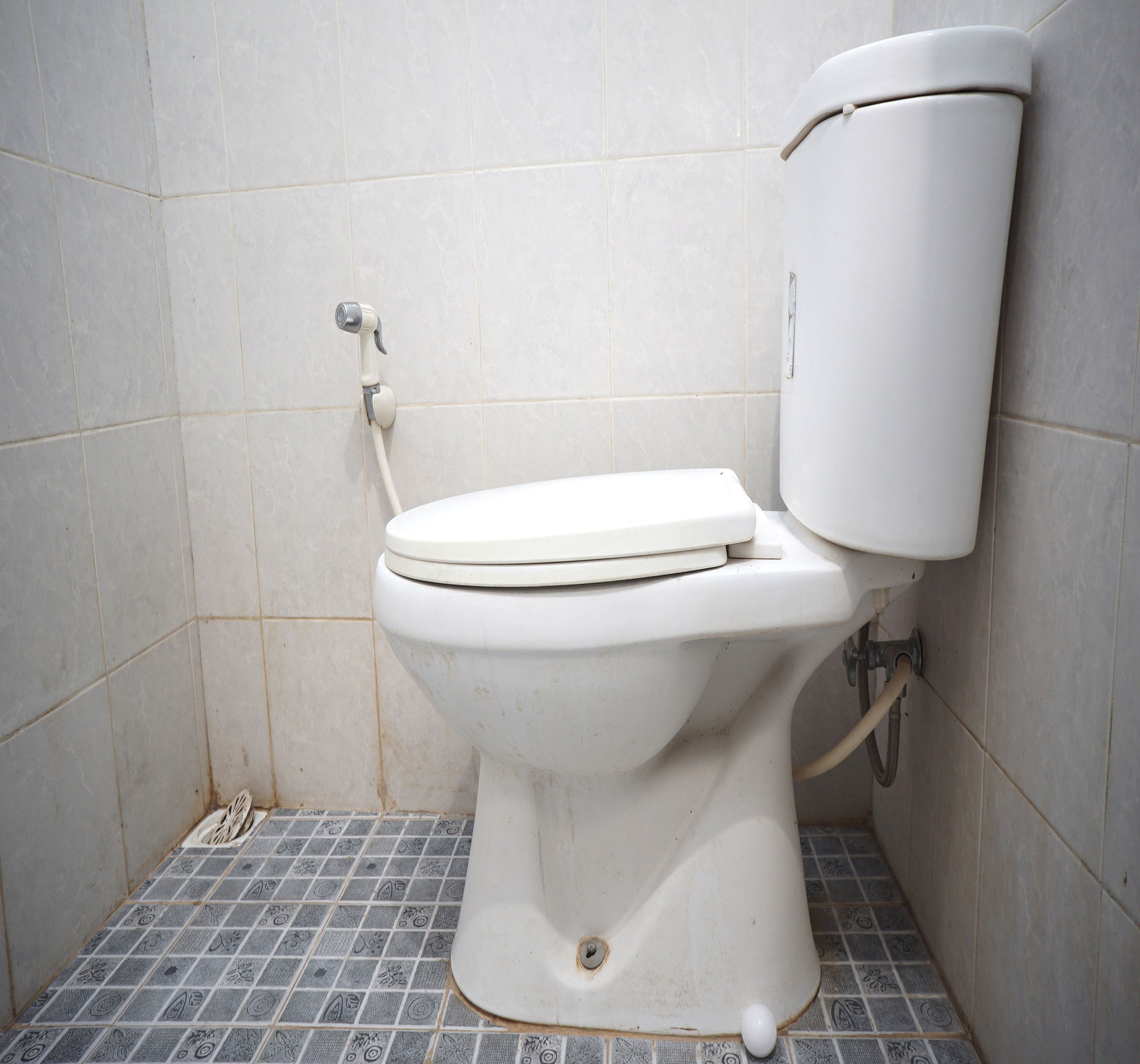 A white toilet with a tank, a bidet attachment, and a tiled floor.