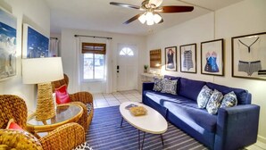 A living room with wicker furniture, a blue sofa, and framed artwork on the walls. - Beachside Cottage - 5 min walk to the Beach (Cocoa Beach)