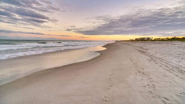 A beach with a wide sandy shore, gentle waves, and a sunset sky. - Beachside Cottage - 5 min walk to the Beach (Cocoa Beach)