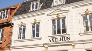 Ein Gebäude mit der Aufschrift "AXELHUS" auf der Fassade, das klassische architektonische Elemente wie Säulen und dekorative Gesimse zeigt.