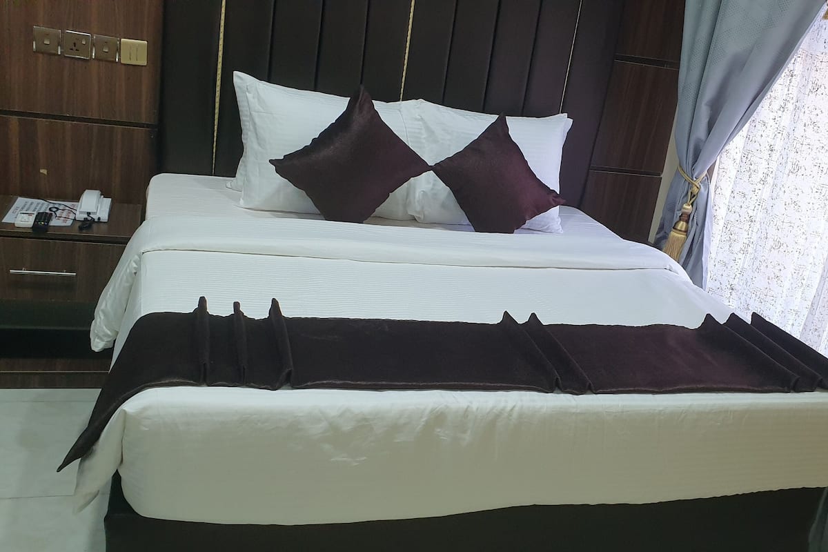 A neatly made bed with white and dark pillows, a dark headboard, and a wooden nightstand with a phone and papers.