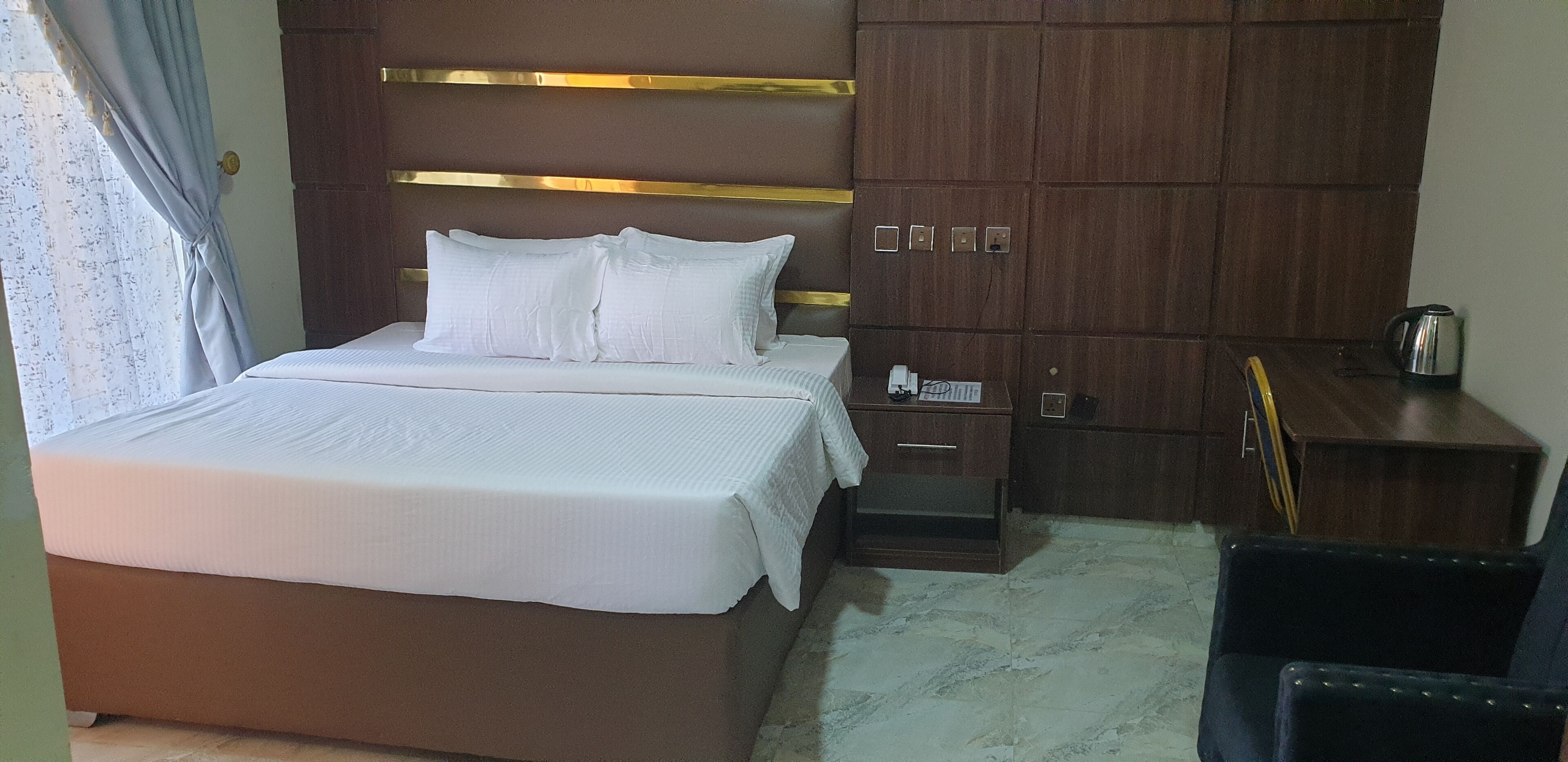 Una habitación de hotel con una cama grande, un armario de madera, un escritorio con hervidor y una silla.