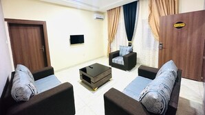 A living room with two sofas, a coffee table, and a TV. There is a door on the left and a sign on the right. - Davina hill resorts and hotel  (Abuja)