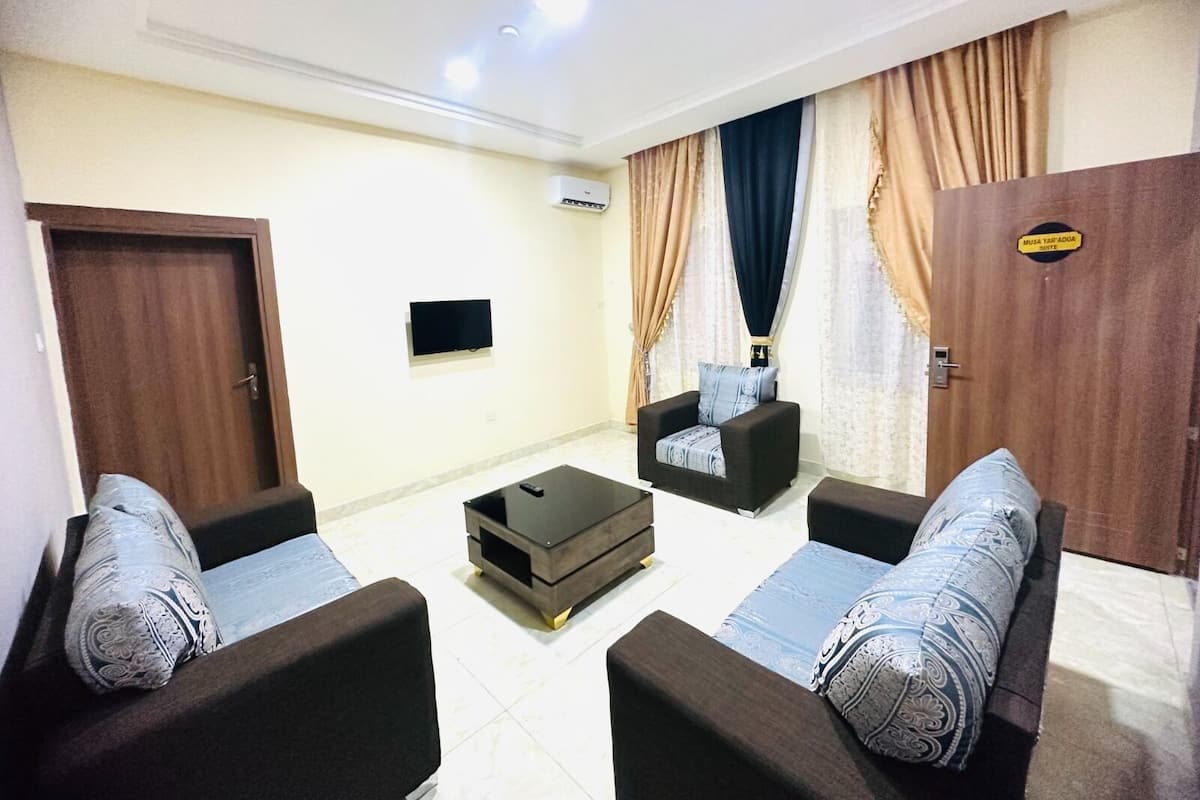 A living room with two sofas, a coffee table, and a TV. There is a door on the left and a sign on the right.
