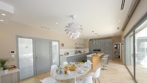 A modern kitchen with a dining area, featuring a round table, white chairs, and a central island with bar stools. - Une Villa Luxueuse à Saint Remy de Provence , A 5 Minutes du Centre , au Calme (Saint-Rémy-de-Provence)