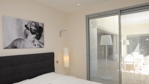 A modern hotel room with a large bed, a wall-mounted artwork, a sliding glass door leading to a balcony, and a small table with a lamp. - Une Villa Luxueuse à Saint Remy de Provence , A 5 Minutes du Centre , au Calme (Saint-Rémy-de-Provence)