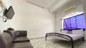 A room with a bed, a sofa, a television mounted on the wall, and a window with a purple curtain. - Hotel O California (Batam)