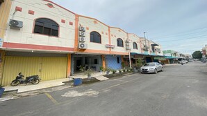 A row of buildings with a yellow garage door, a silver car parked on the street, and several potted plants along the sidewalk. - Hotel O California (Batam)
