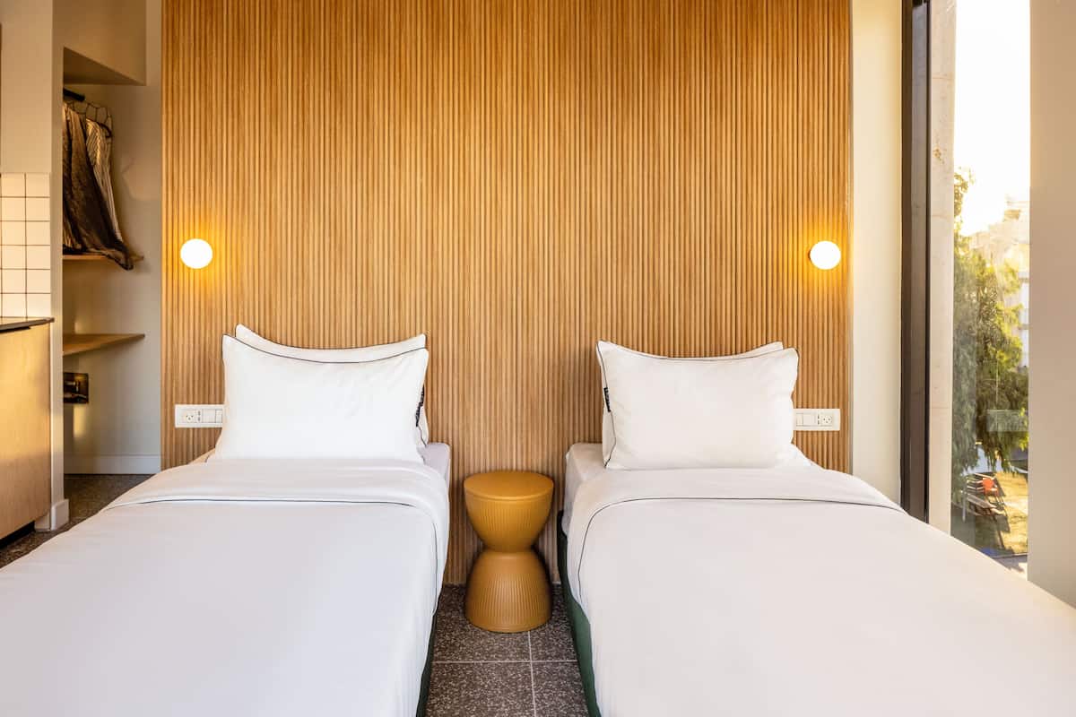 Ein Hotelzimmer mit zwei Betten, einer Wand aus Holzpaneelen und einem kleinen, runden Hocker.