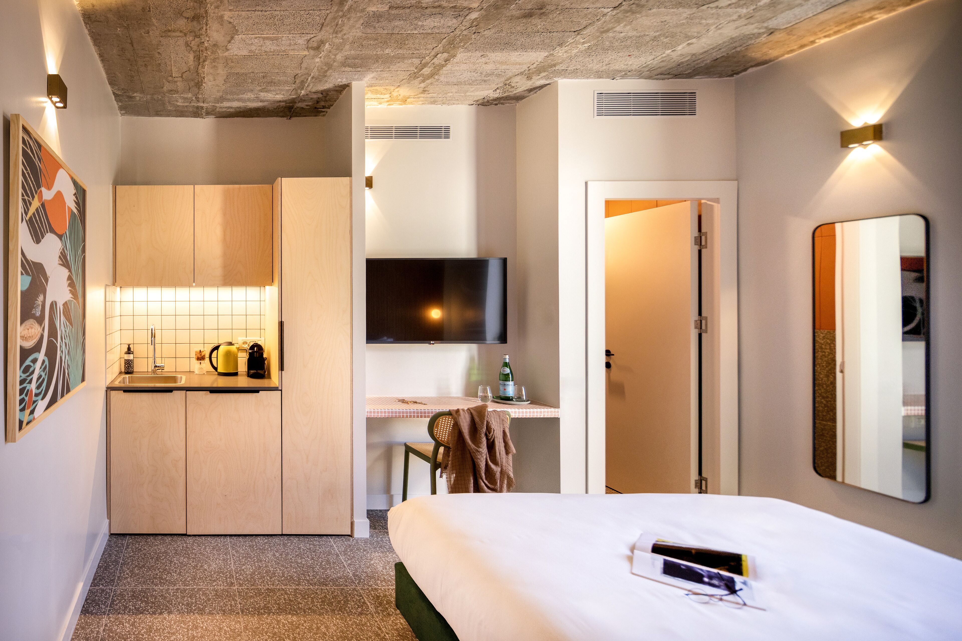 Una habitación de hotel con cama, escritorio, televisor y kitchenette.