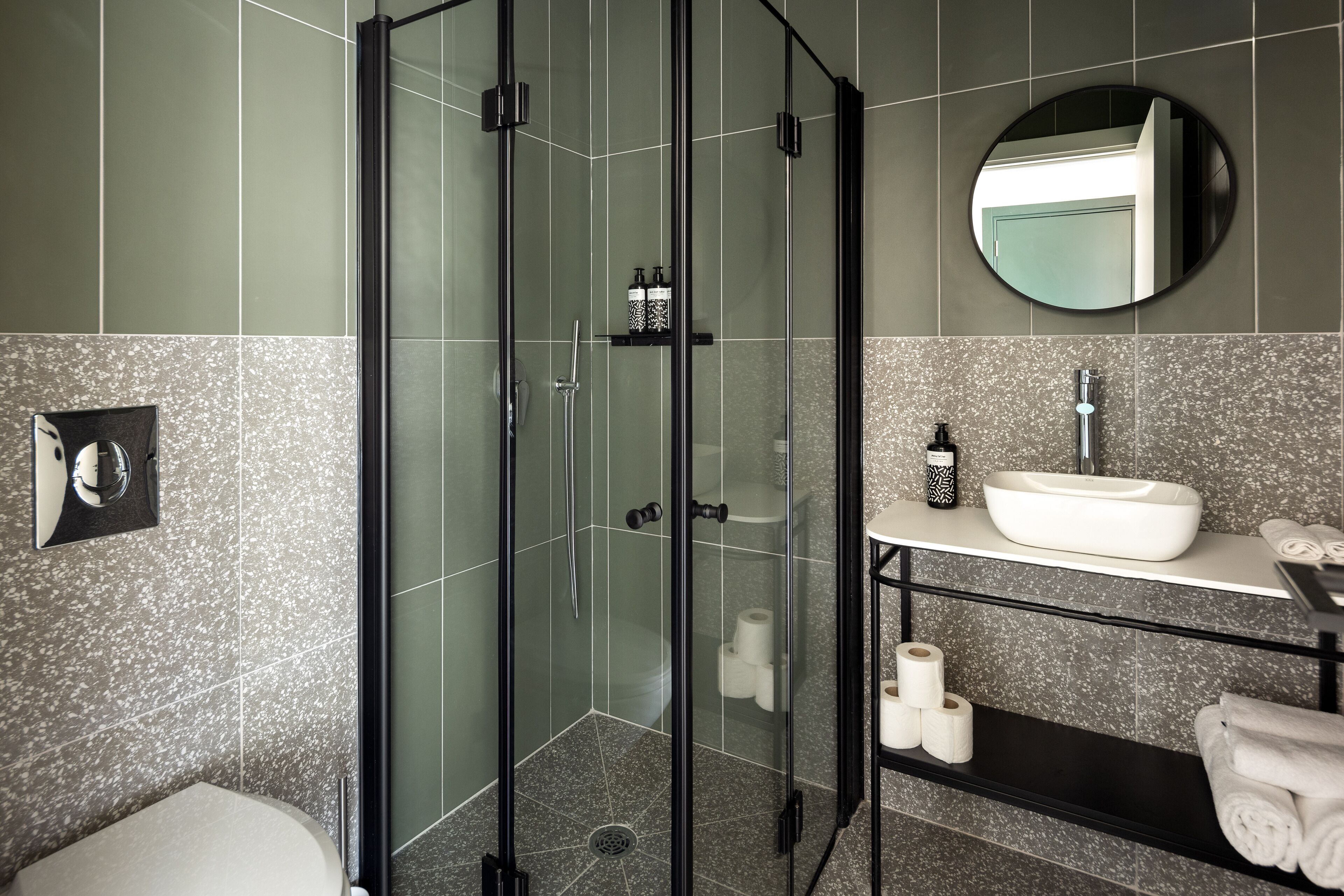 Un baño moderno con ducha de vidrio, un lavabo blanco y un espejo redondo.