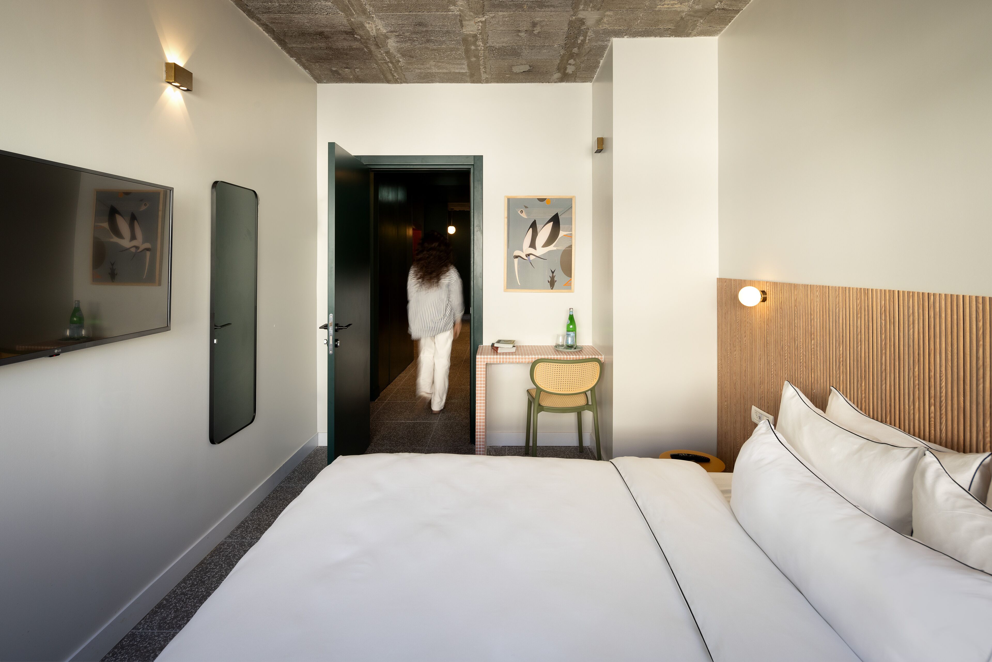 A hotel room with a large bed, a desk with a chair, a mirror, and artwork on the walls.