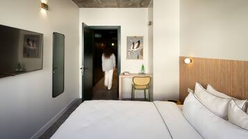 A hotel room with a large bed, a desk with a chair, a mirror, and artwork on the walls.