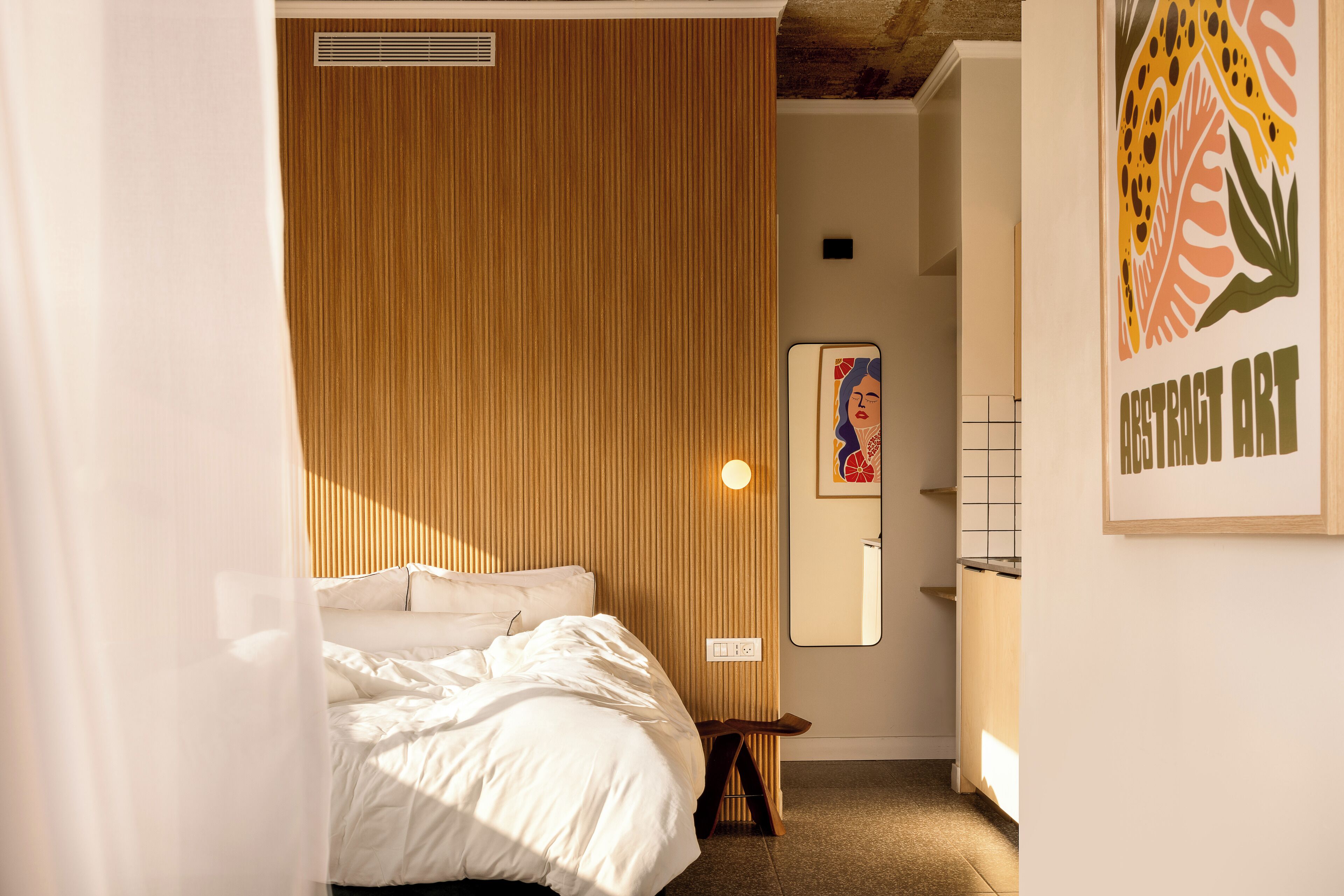 A bedroom with a wooden headboard, a bedside table, a mirror, and a framed abstract art piece on the wall.