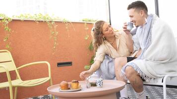 A couple sitting at a table with a cup of coffee, a muffin, and a teapot.