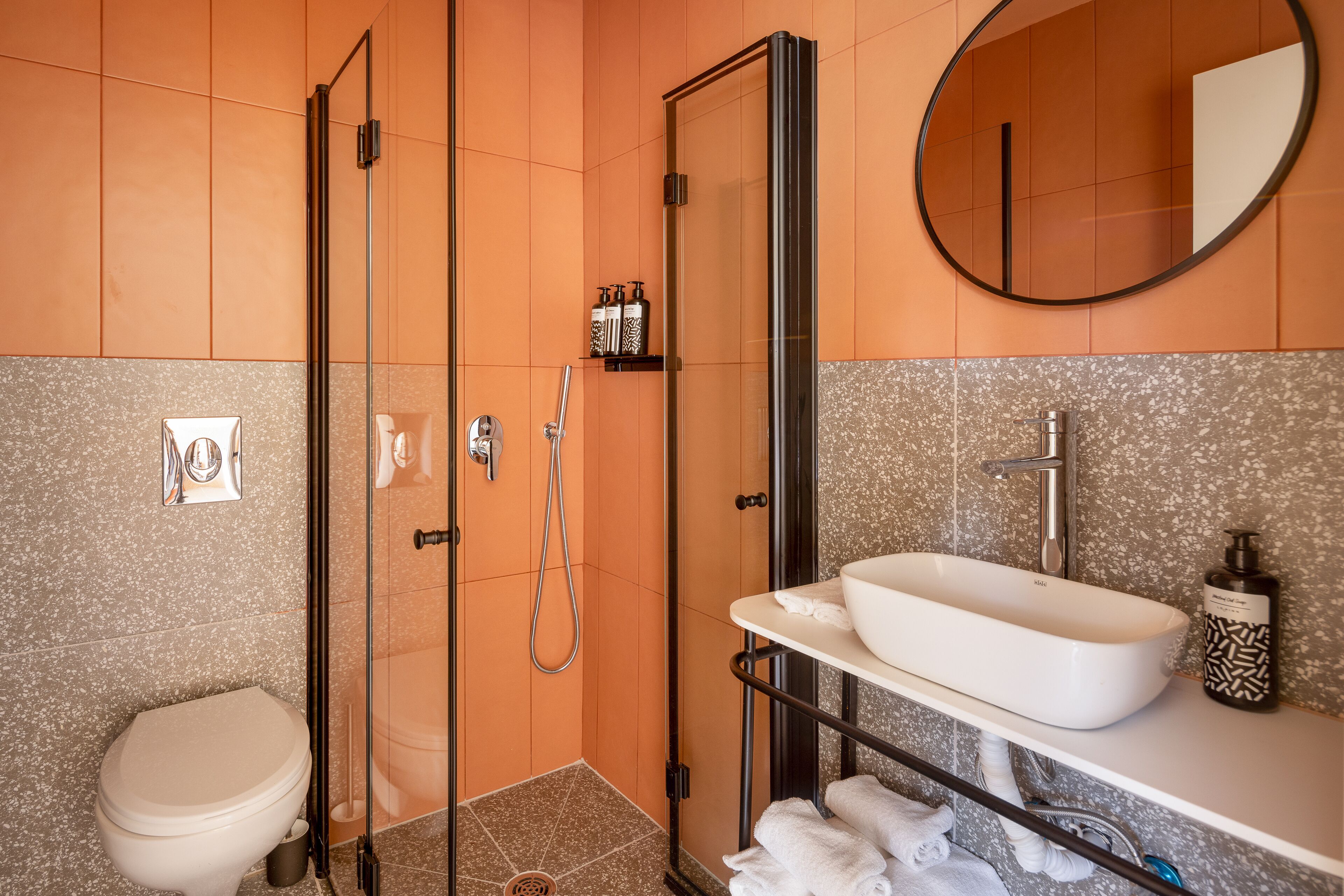 A modern bathroom with a glass-enclosed shower, a white sink, and a round mirror.
