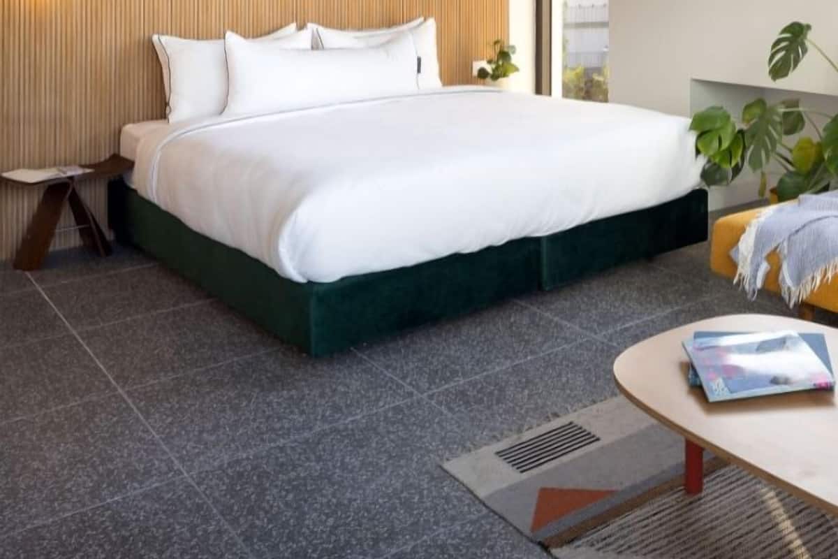 Ein modernes Hotelzimmer mit einem großen Bett, einem kleinen Nachttisch, einem runden Couchtisch und Blick ins Freie durch ein Fenster.