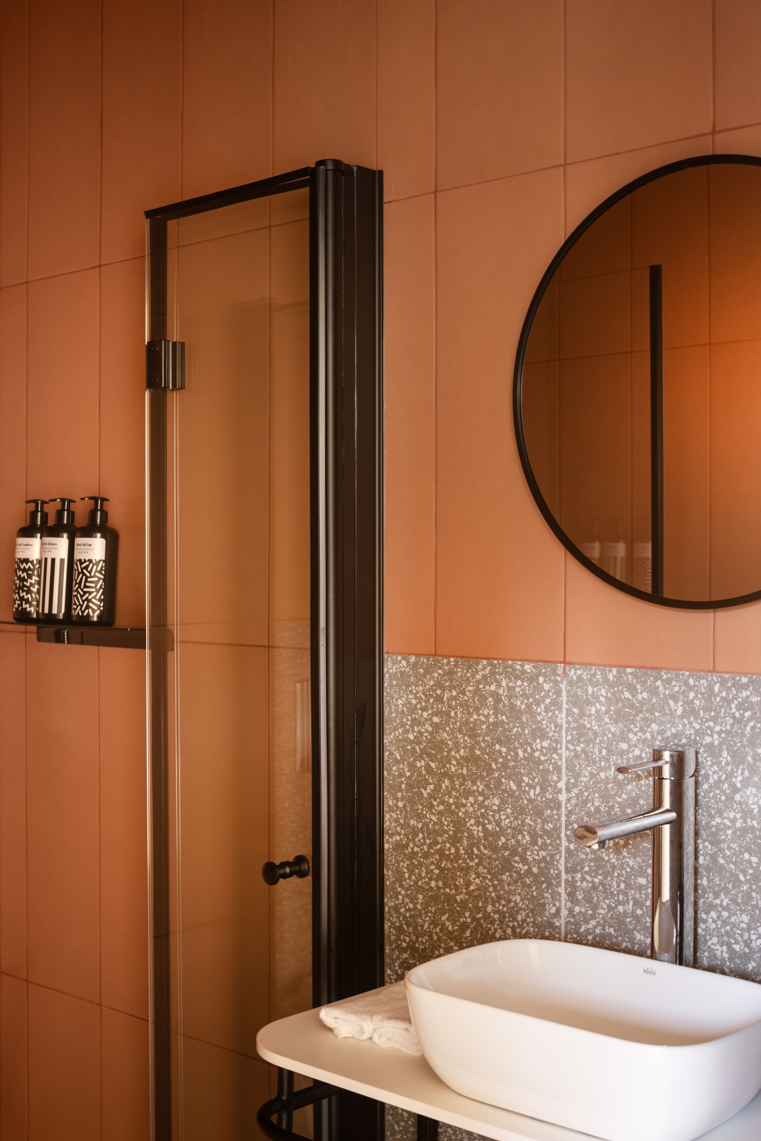 A bathroom with a glass-enclosed shower, a round mirror, and a white sink.
