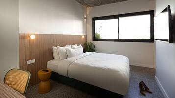 A bedroom with a bed, a chair, a small table, a window, and a plant.