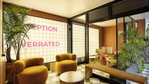 A reception area with a checkered floor, two yellow armchairs, a wooden bench, and a large potted plant. - Savanna Dizengoff - Smart Hotel by Loginn Tel Aviv (Tel Aviv)