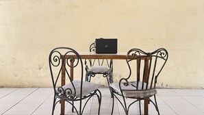 A dining area with a table and two chairs, a laptop on the table, and a wall with five square windows. - OYO Life 93398 Sudimoro Guest House Syariah (Malang)