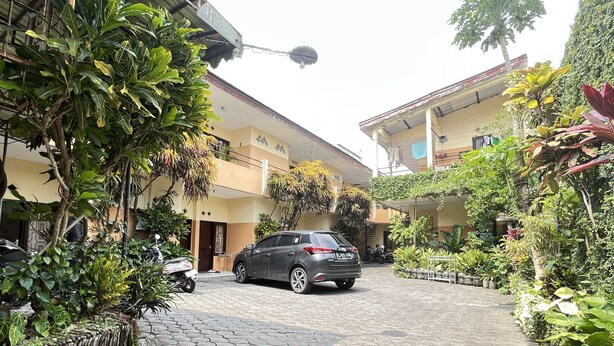 A paved courtyard with a parked car, surrounded by lush greenery and a building with multiple balconies. - OYO Life 93398 Sudimoro Guest House Syariah (Malang)