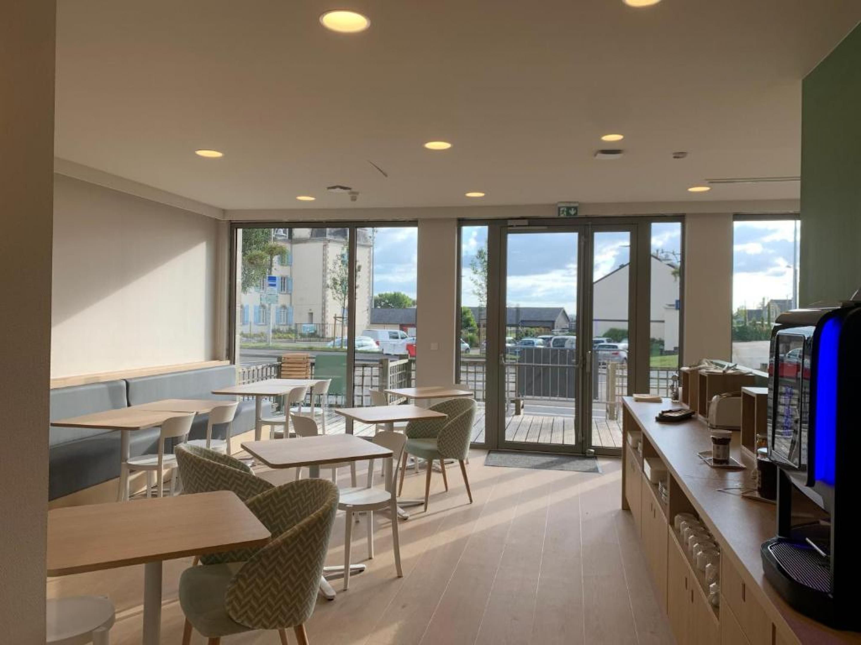 A cafe with tables and chairs, a counter with a coffee machine, and large windows with a view of the street.