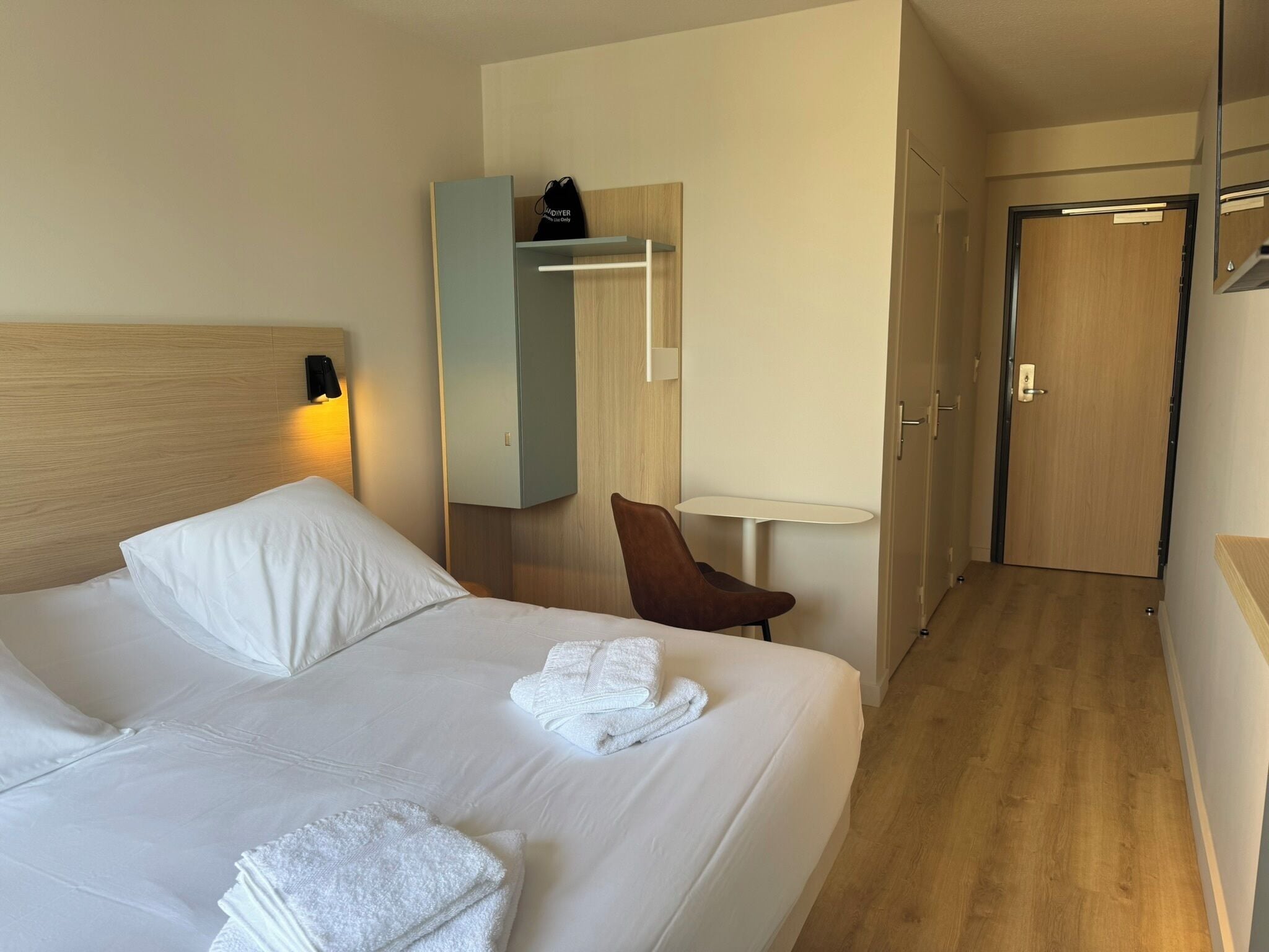 Habitación de hotel con cama, una silla, una mesita, armario y puerta.