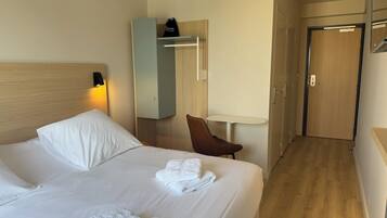 Habitación de hotel con cama, una silla, una mesita, armario y puerta.