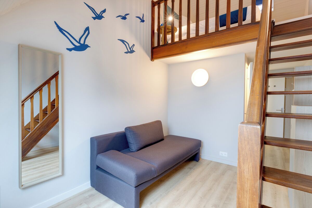 Ein Zimmer mit grauem Sofa, einer Holztreppe und einer Wand mit Vogelaufklebern.
