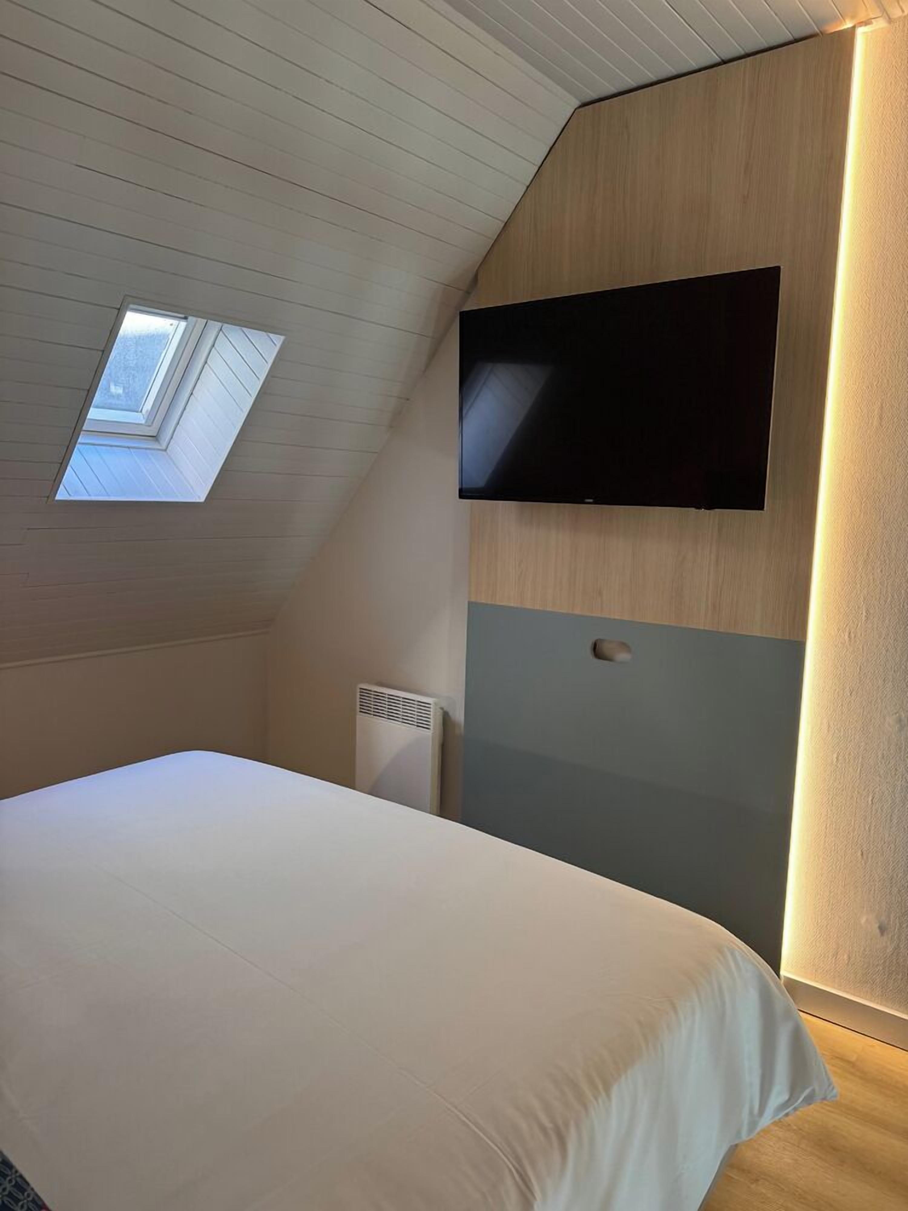 A bedroom with a sloped ceiling, a skylight, a bed, a wall-mounted TV, and a radiator.