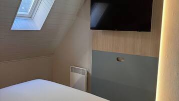 A bedroom with a sloped ceiling, a skylight, a bed, a wall-mounted TV, and a radiator.