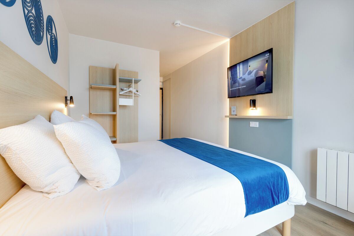 Una habitación de hotel moderna con cama, televisor montado en la pared y armario empotrado.