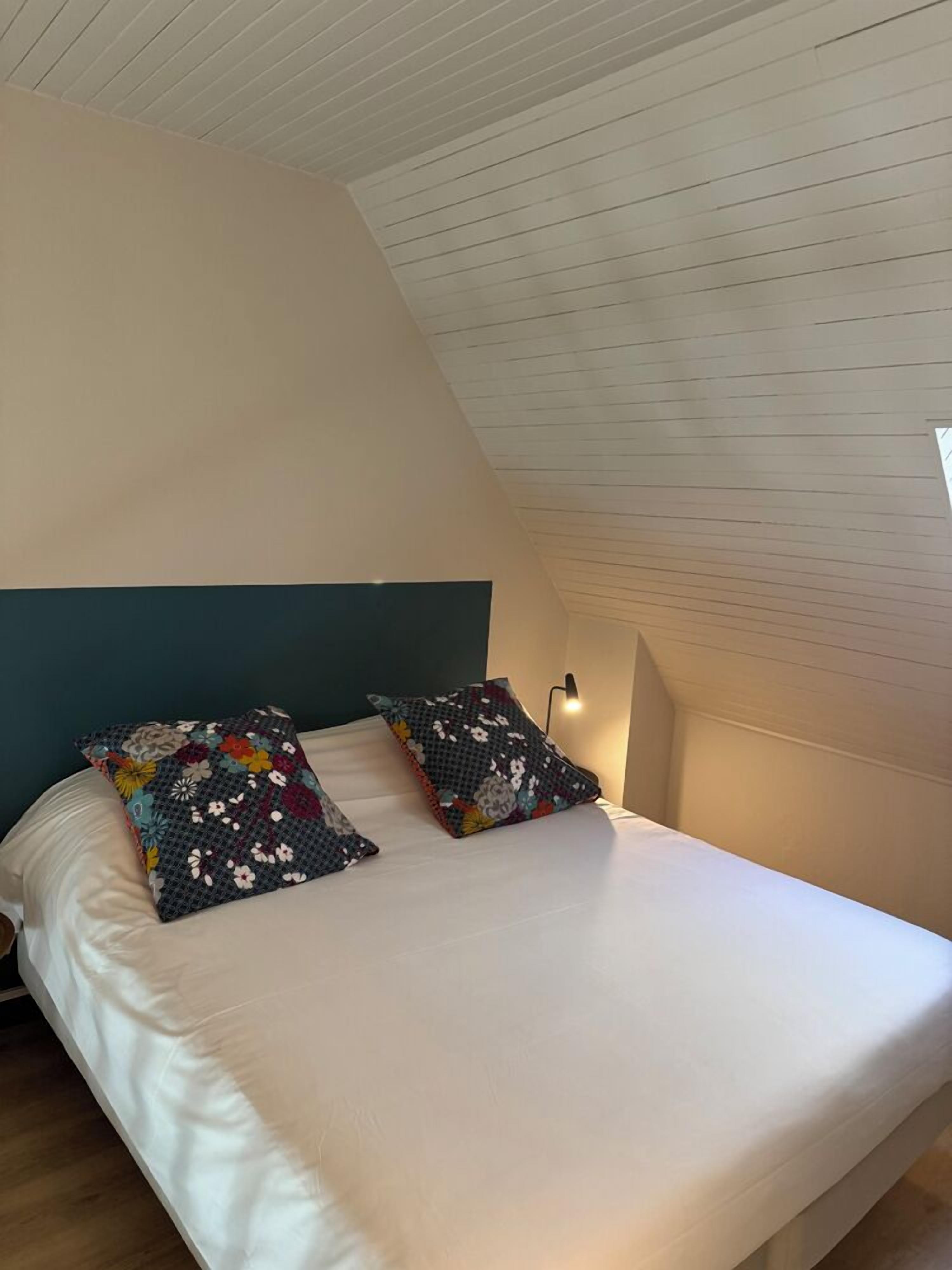 A bedroom with a sloped ceiling, a bed with white bedding, and two decorative pillows.