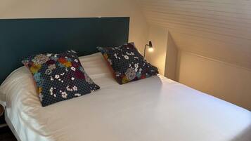 A bedroom with a sloped ceiling, a bed with white bedding, and two decorative pillows.