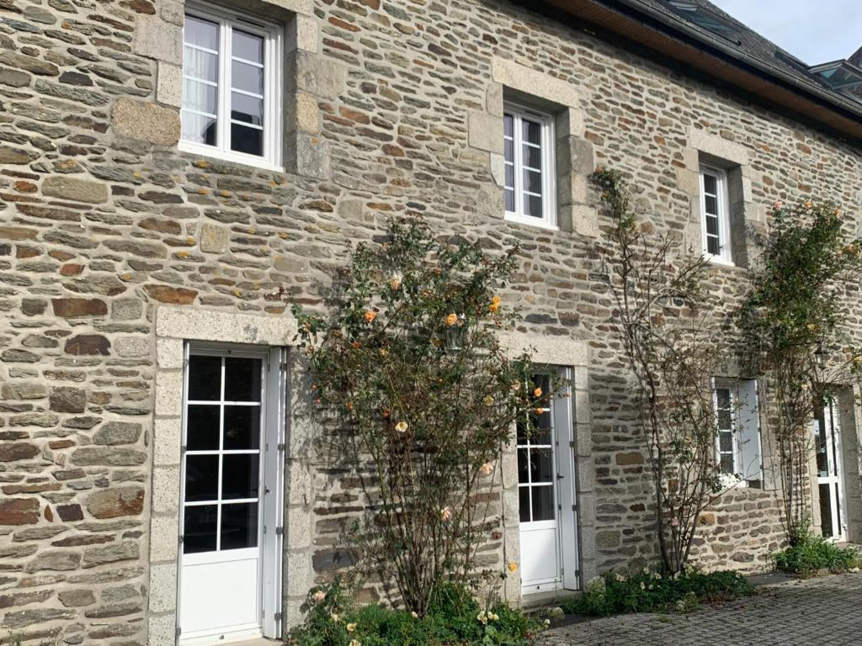A stone building with multiple windows and doors, surrounded by greenery.