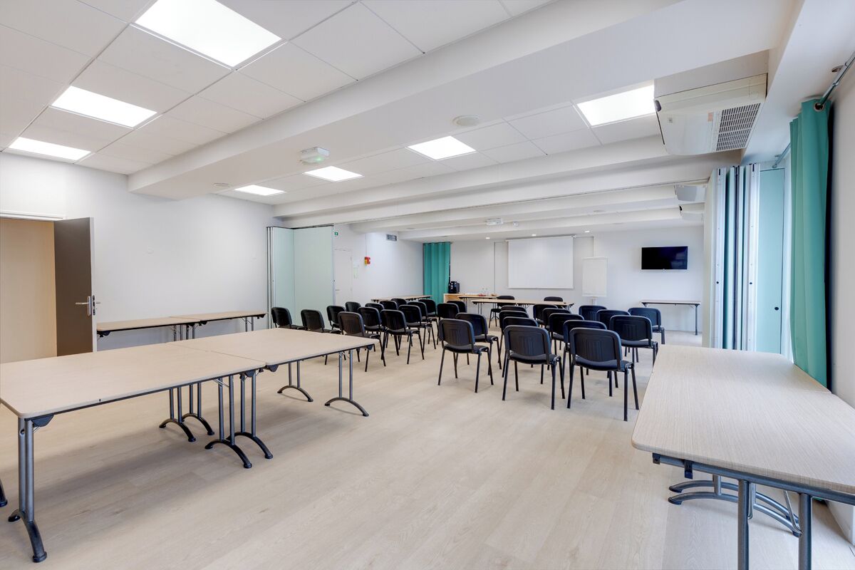Un salón de conferencias con una larga mesa, sillas, una pizarra y una pantalla para proyector.